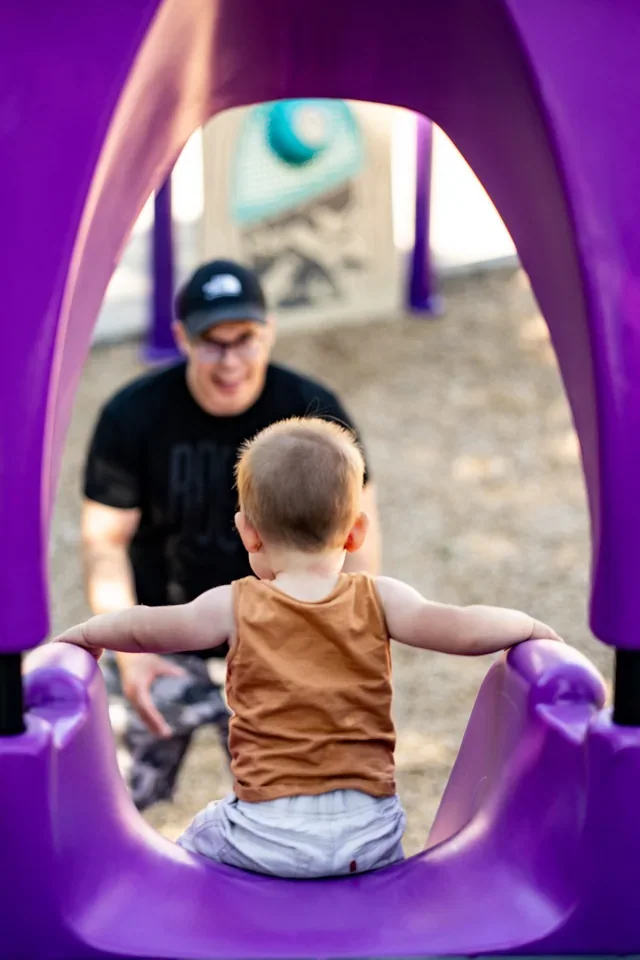 A child in a purple playground tunnel reaching toward an adult