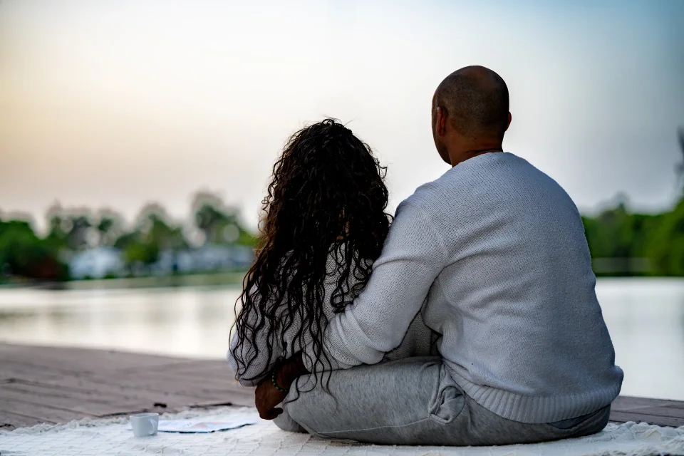 Two people sitting side by side on a dock facing the lake