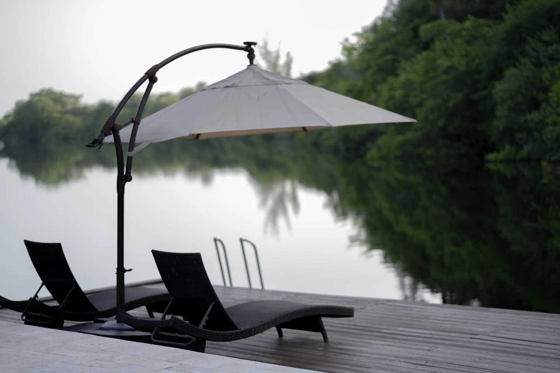 Two lounge chairs and an umbrella on a deck beside a tree-lined lake