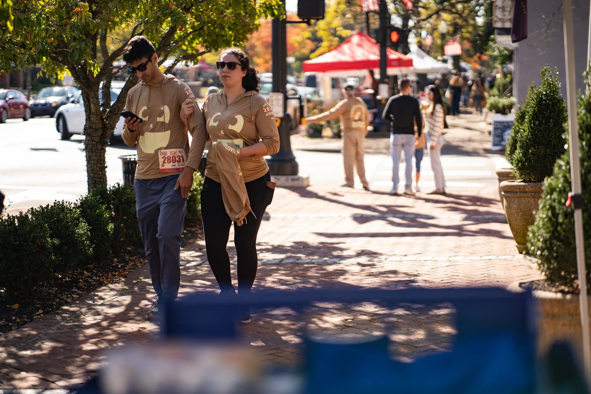 People strolling along a sunlit sidewalk between market tents and shops