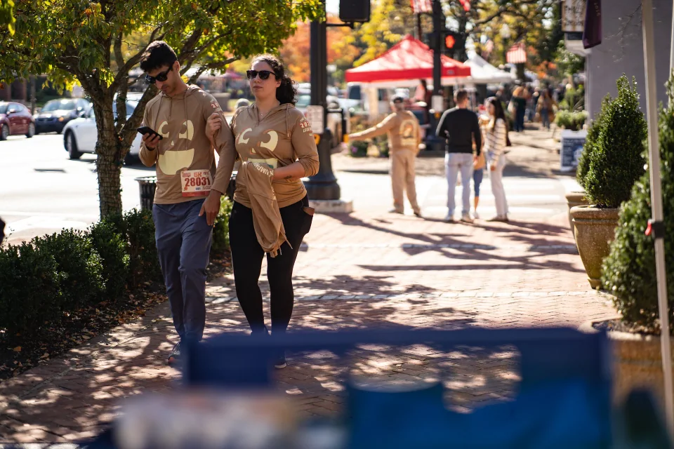 People strolling along a sunlit sidewalk between market tents and shops