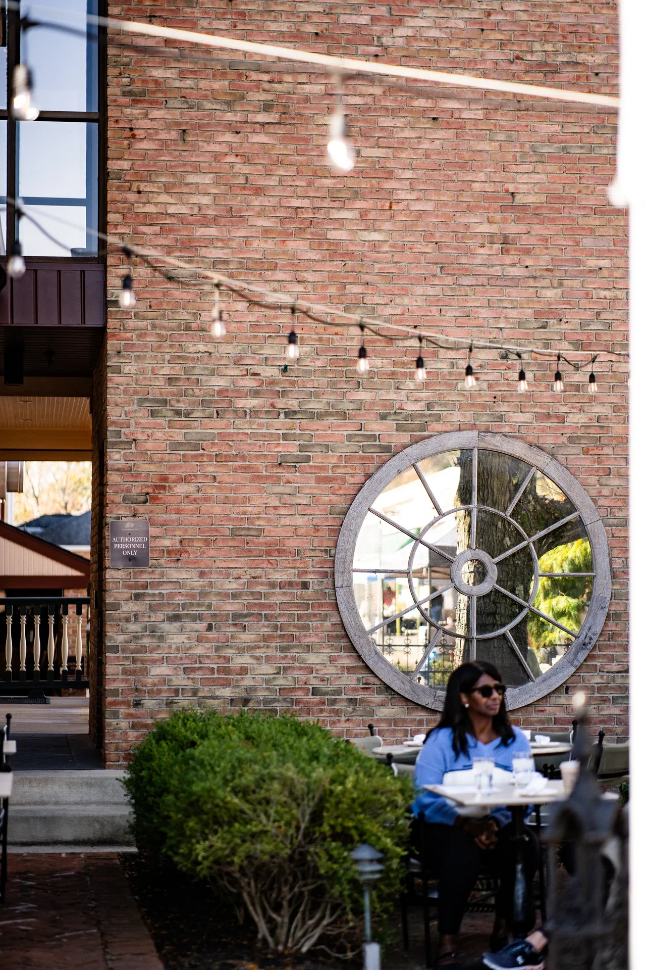 A person seated beside a brick wall with a round window