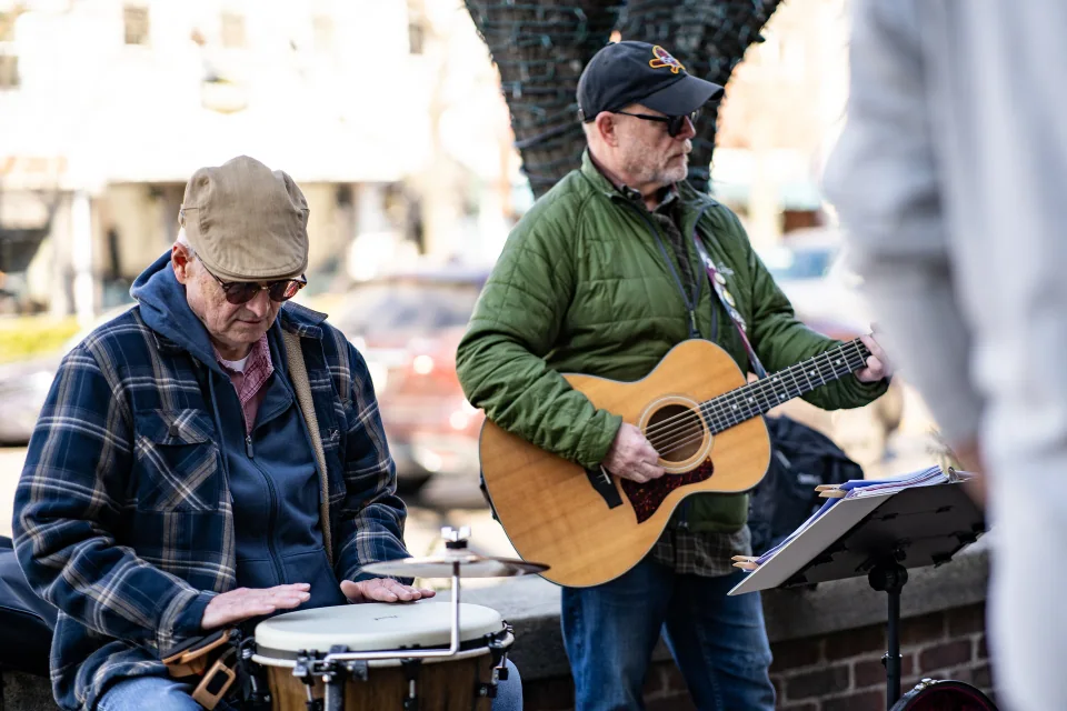 Two street musicians playing guitar and hand drums outdoors