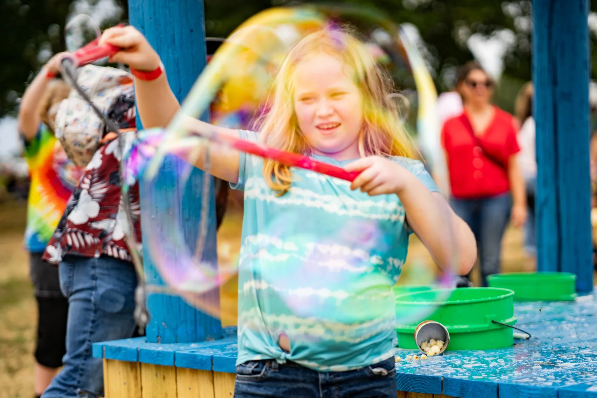 A child making a large iridescent bubble beside colorful playground equipment
