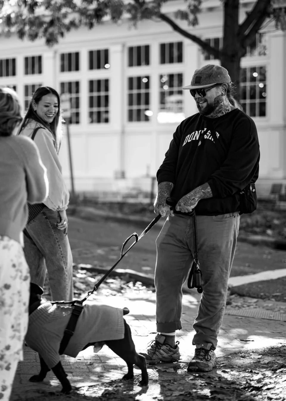 A person standing with a leashed pig on a sunny sidewalk, in black and white