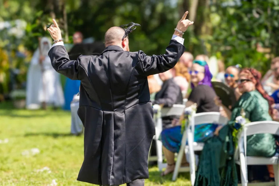 A person in a suit raising both arms toward seated wedding guests