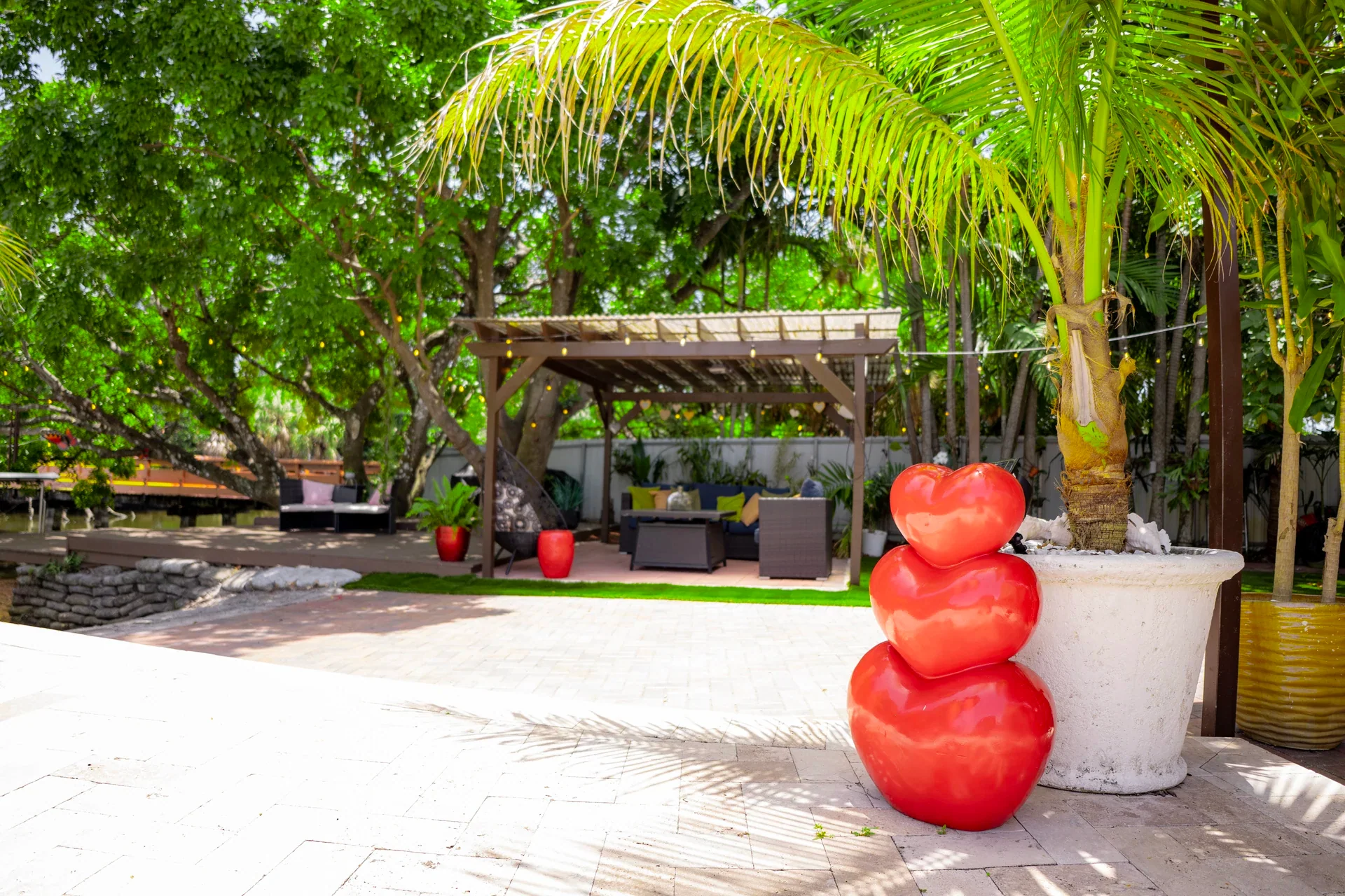 A sunny palm-lined patio with a pergola and a red sculpture