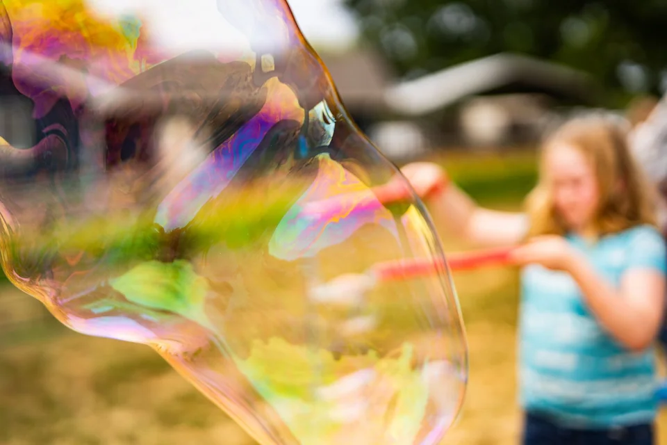 Iridescent bubble filling the foreground as a child makes it behind