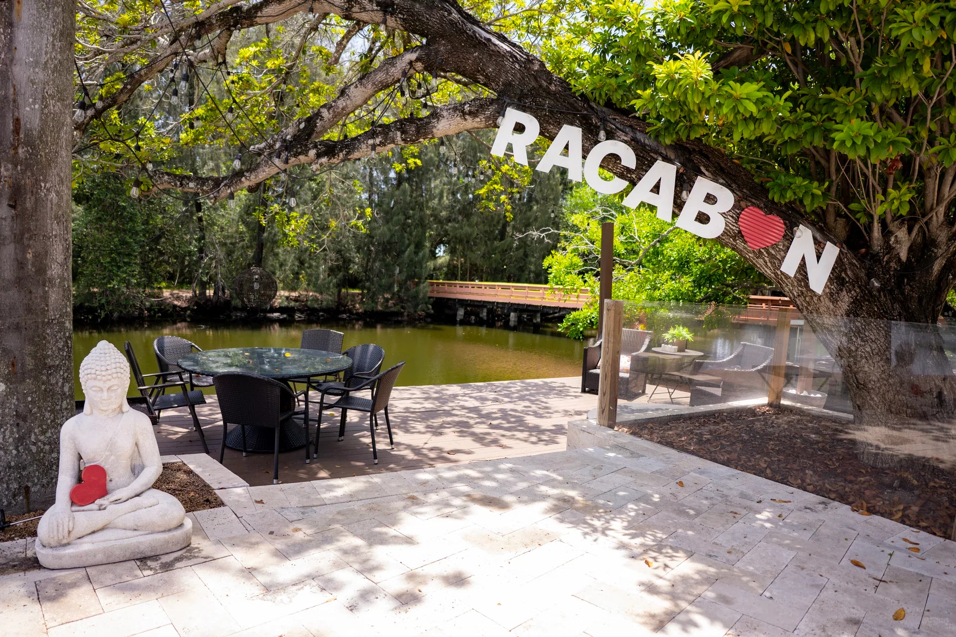 A stone patio beneath leafy trees with a sculpture and hanging letter banner