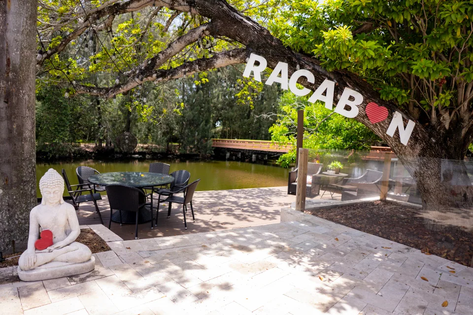 A stone patio beneath leafy trees with a sculpture and hanging letter banner