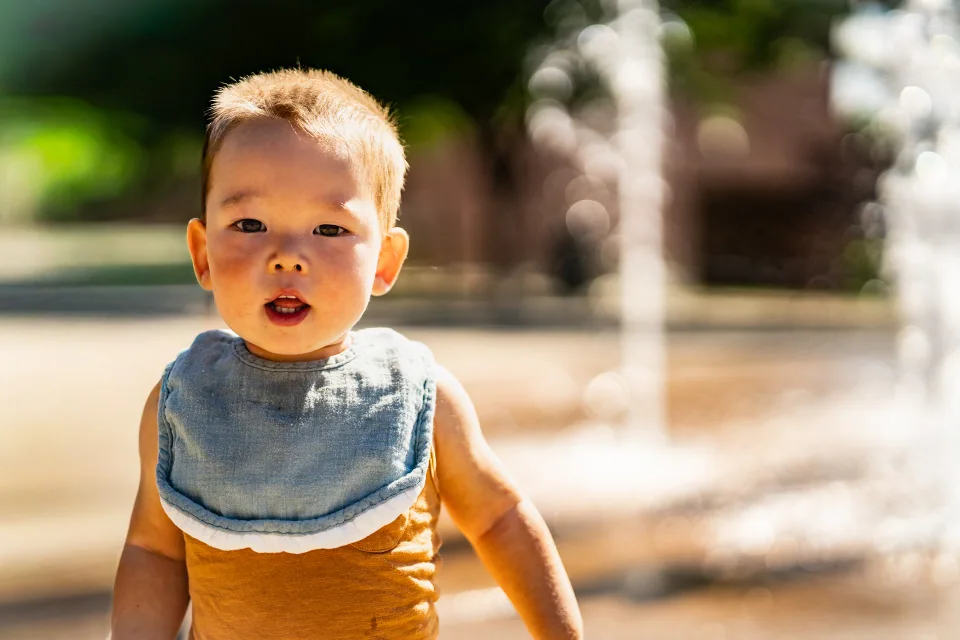 A toddler standing outdoors in a brown outfit and blue bib