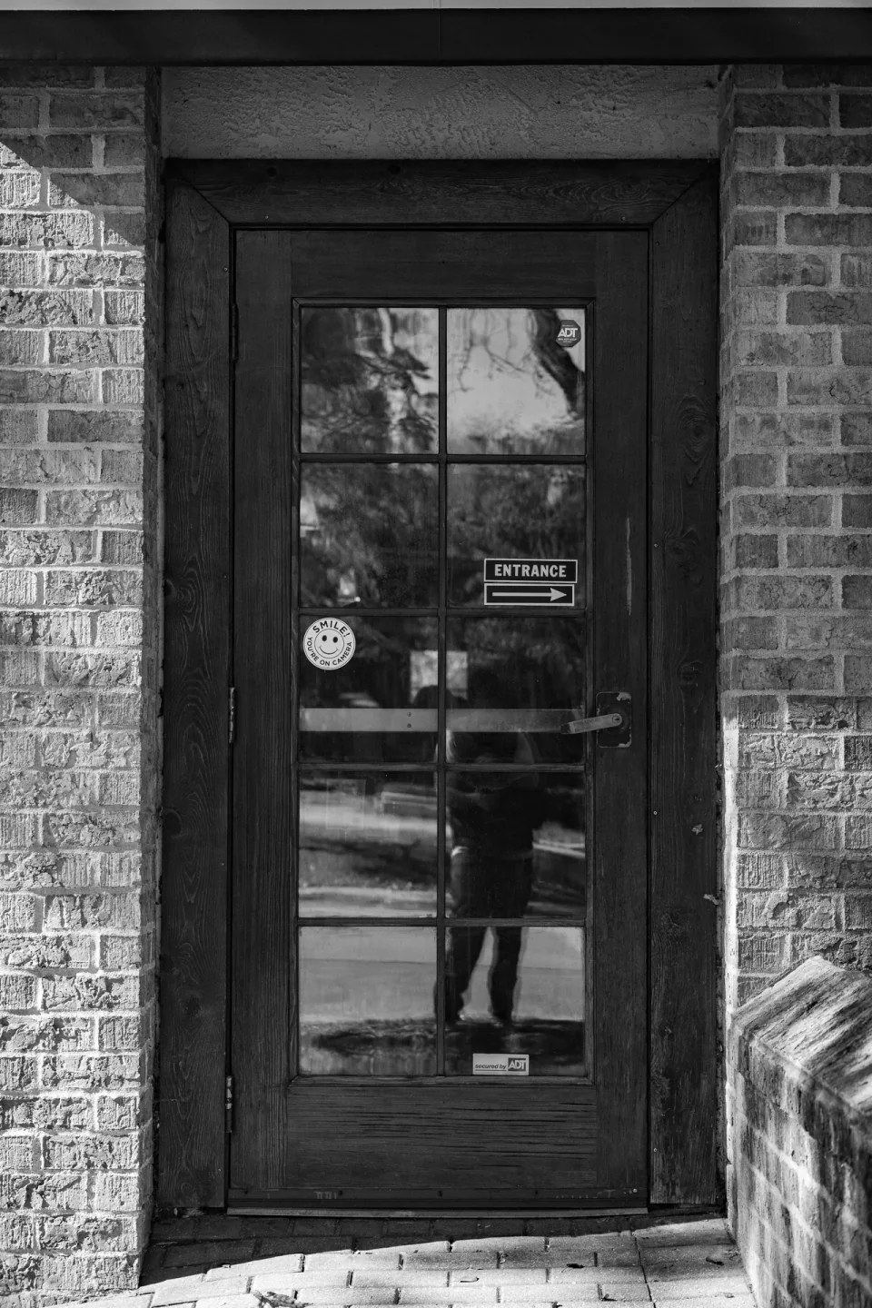 A dark glass shop door framed by brick, photographed in black and white