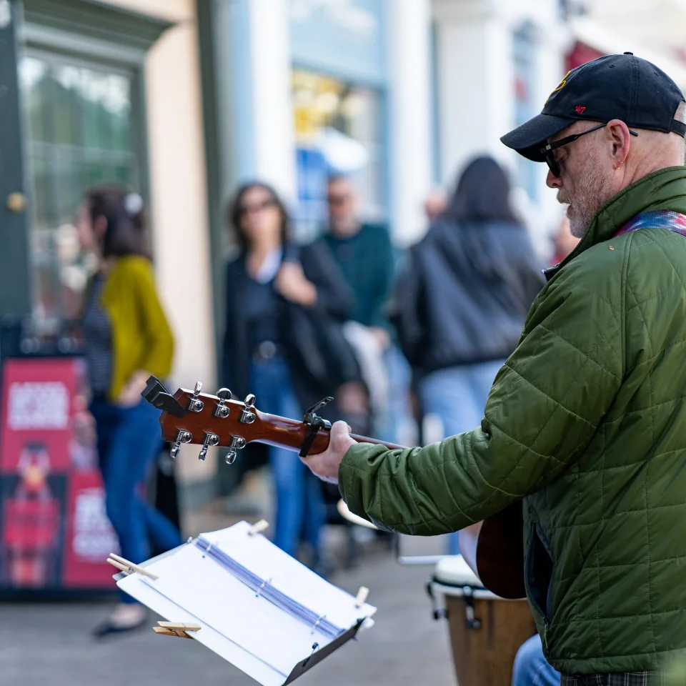 A guitarist seen from the side while performing for passersby