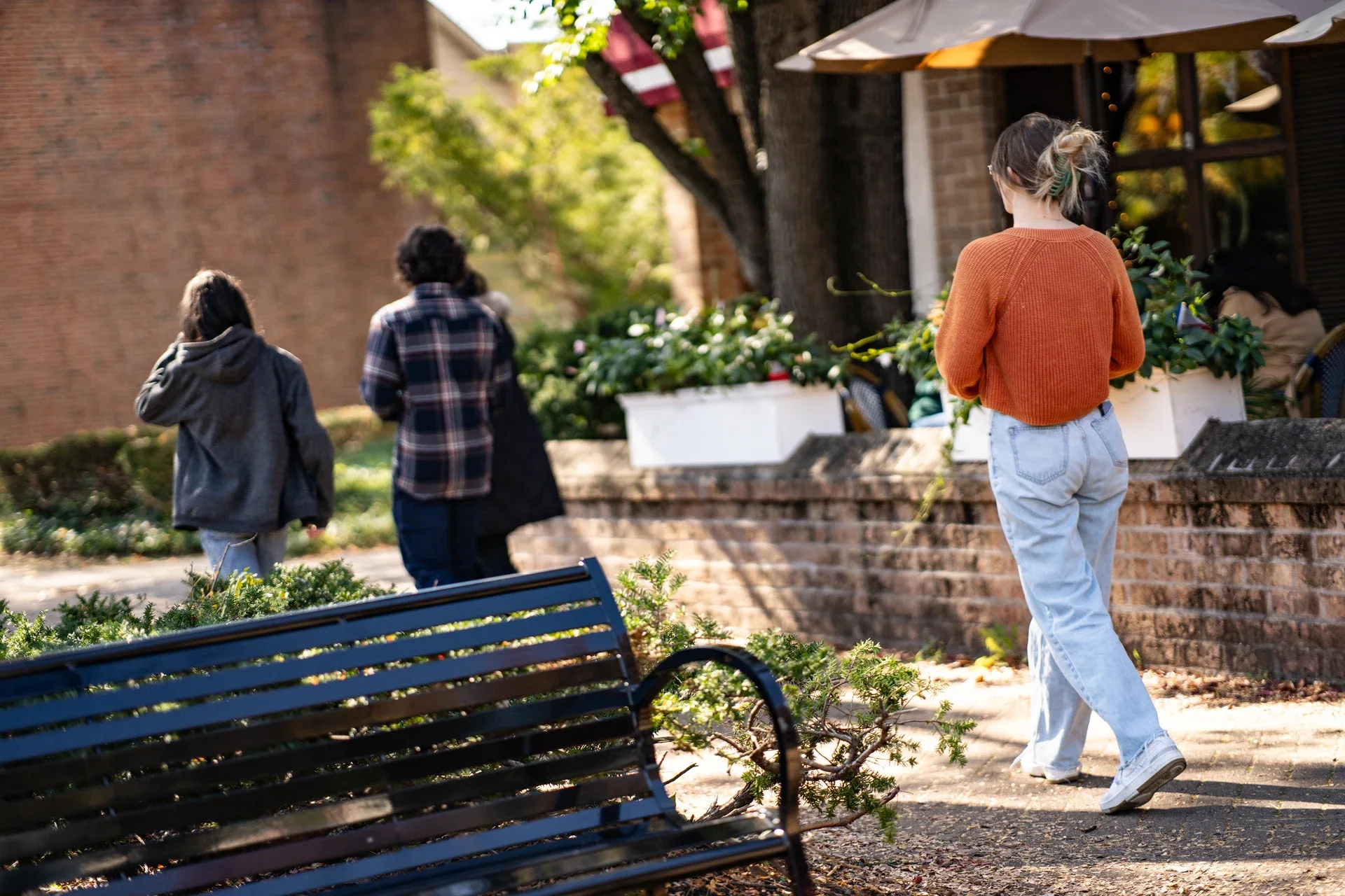 People walking past a blue bench and low brick wall
