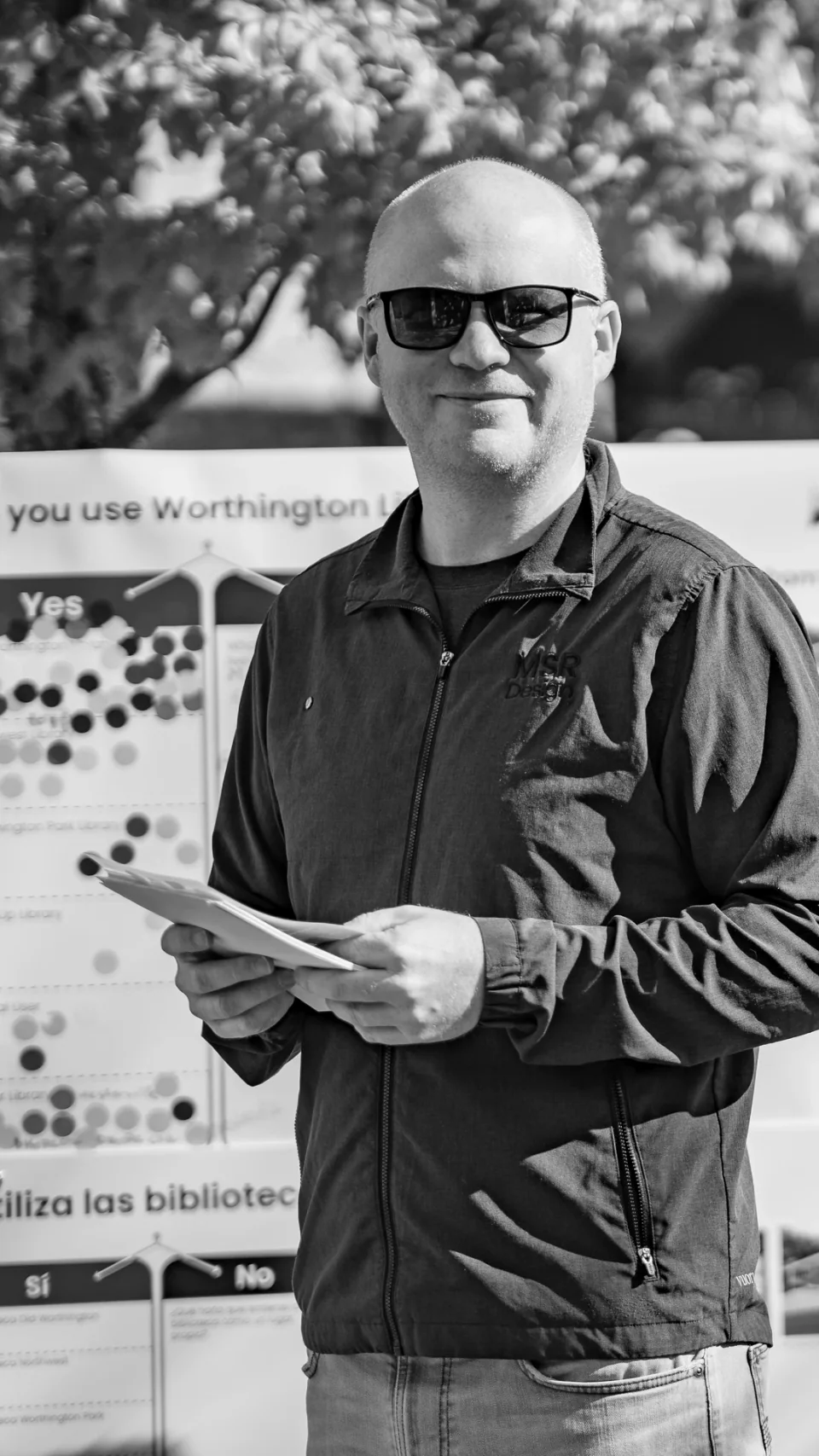 A person holding a leaflet beside an outdoor display, in black and white