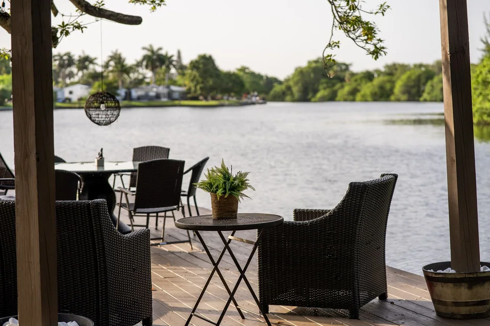 Wicker chairs and a potted fern on a deck overlooking a lake