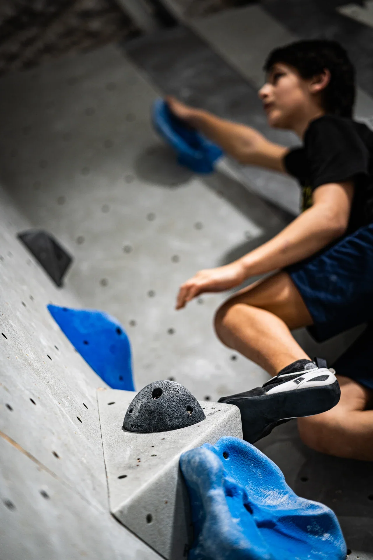 A climber reaching upward on a wall with blue holds