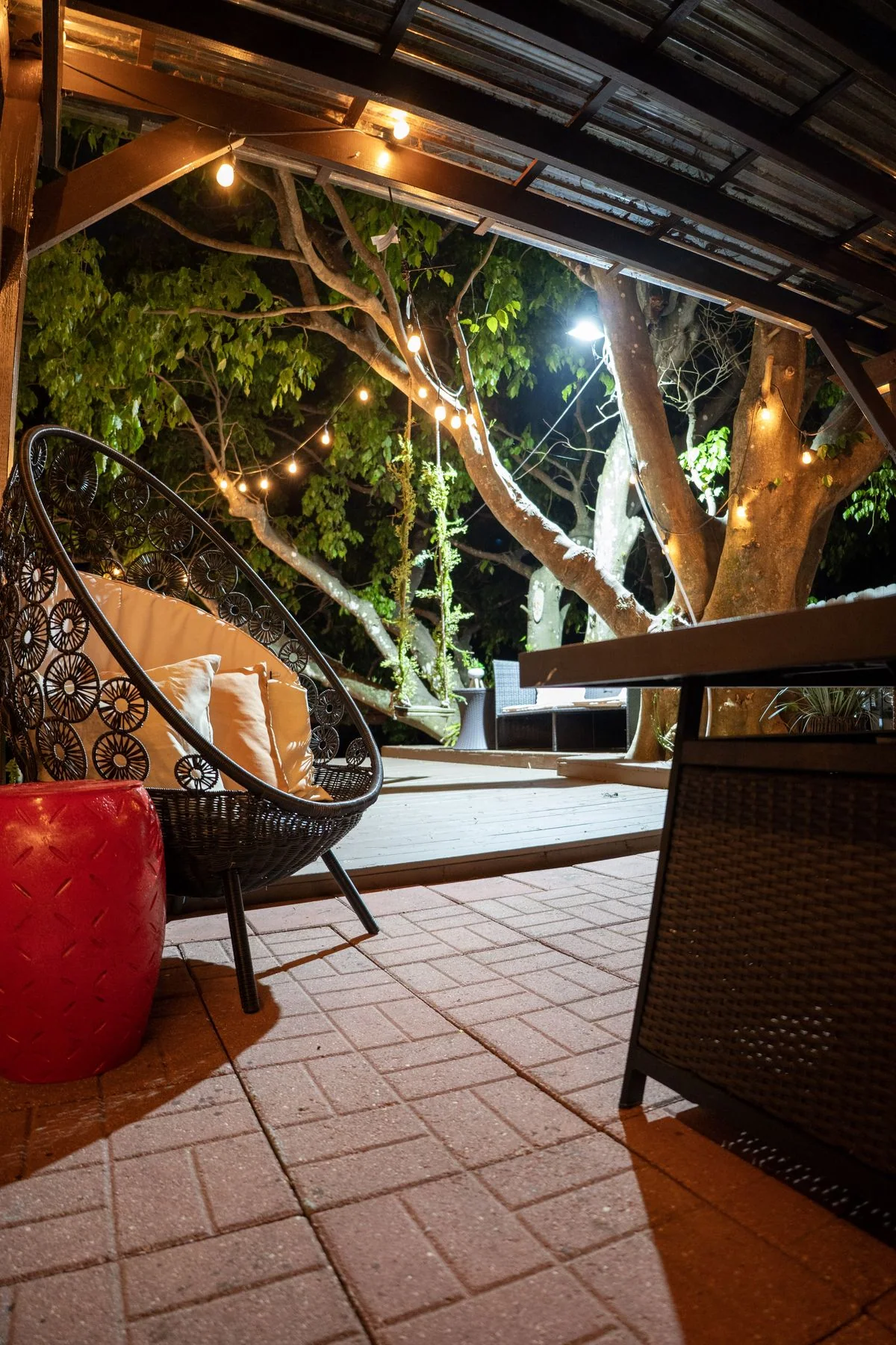 Hanging chair and tree-lit patio beneath a covered roof at night