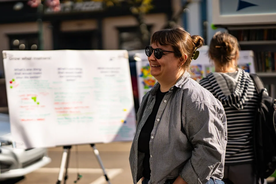 A person smiling beside an outdoor information table and whiteboard