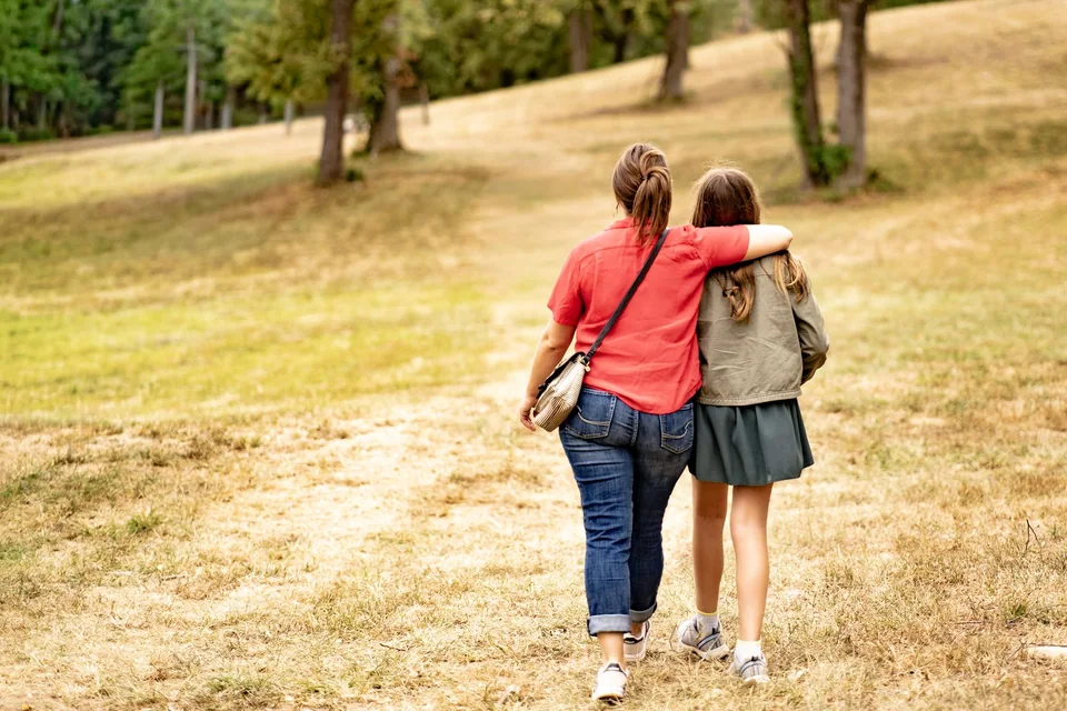 Mother and daughter walking arm in arm through a sunlit field