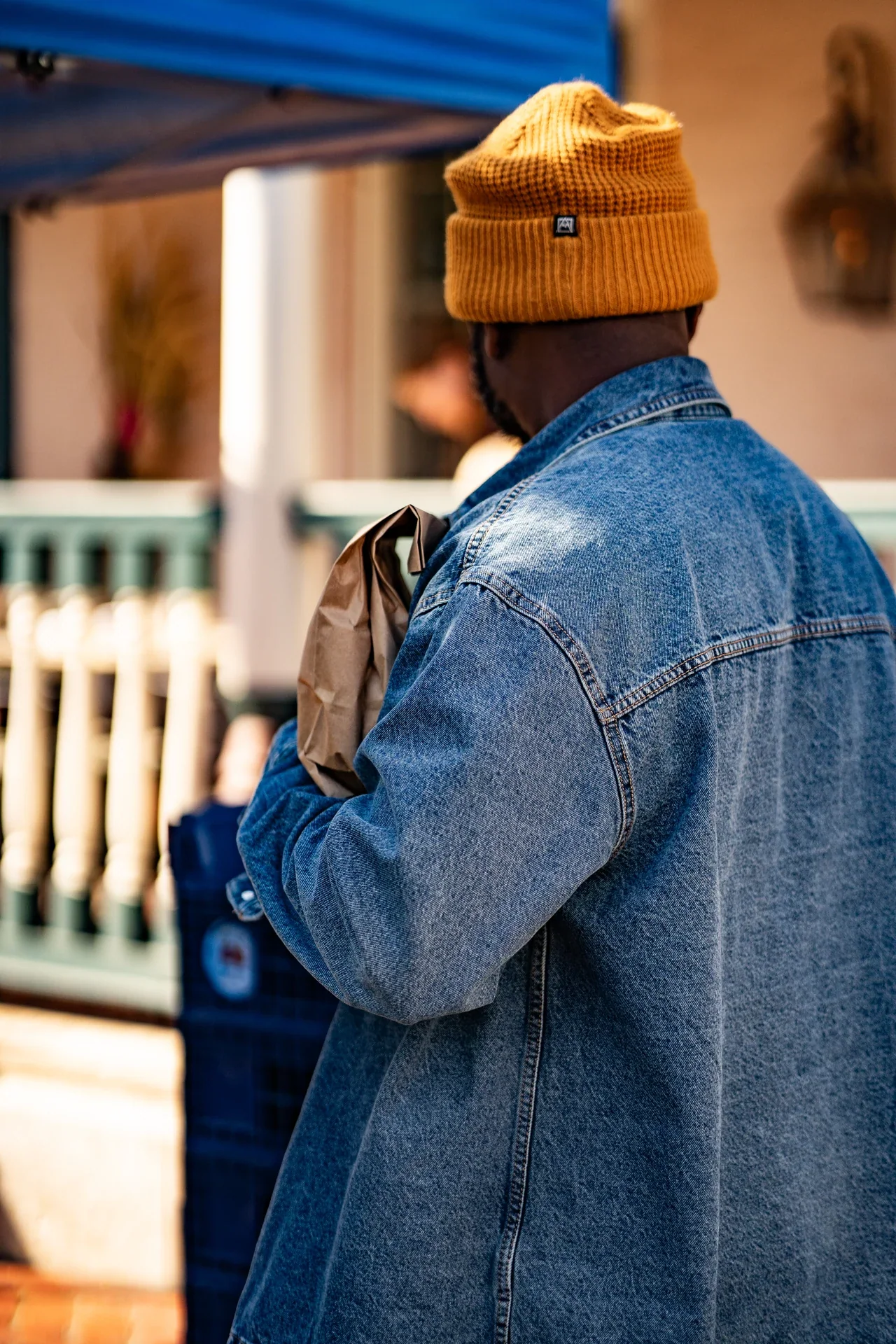 A person in a denim jacket and yellow hat beside a brick wall