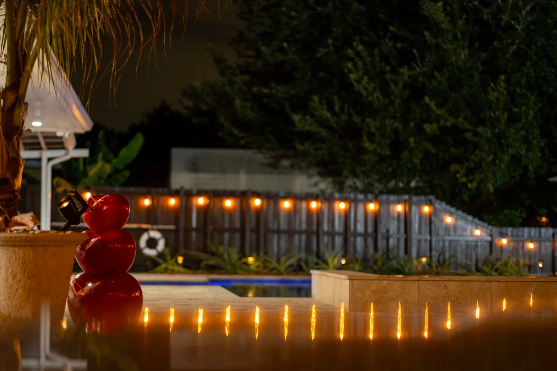A pool at night with warm string lights reflected in the water
