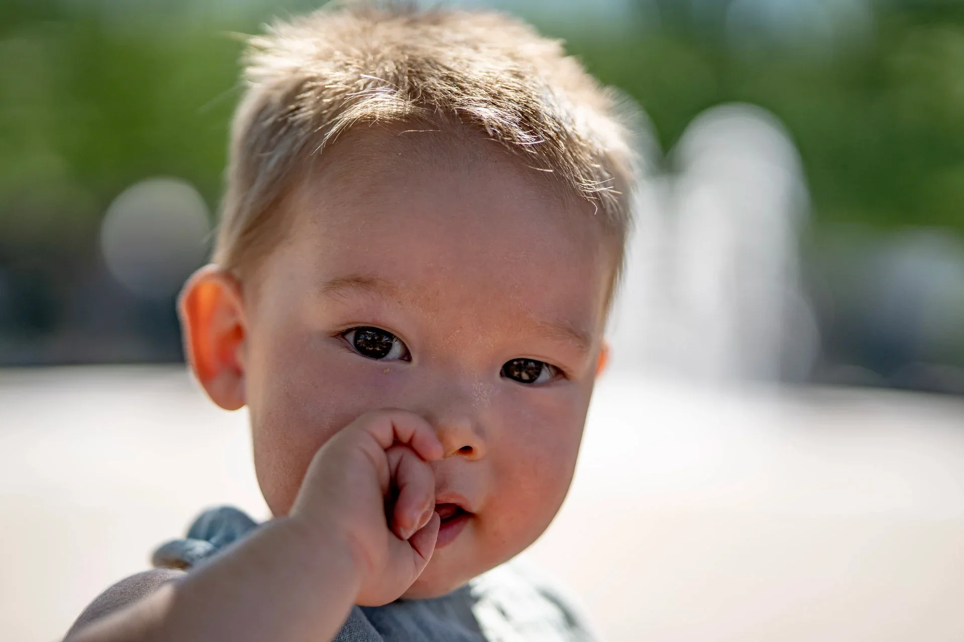 Close-up of a toddler looking toward the camera with a hand near their mouth