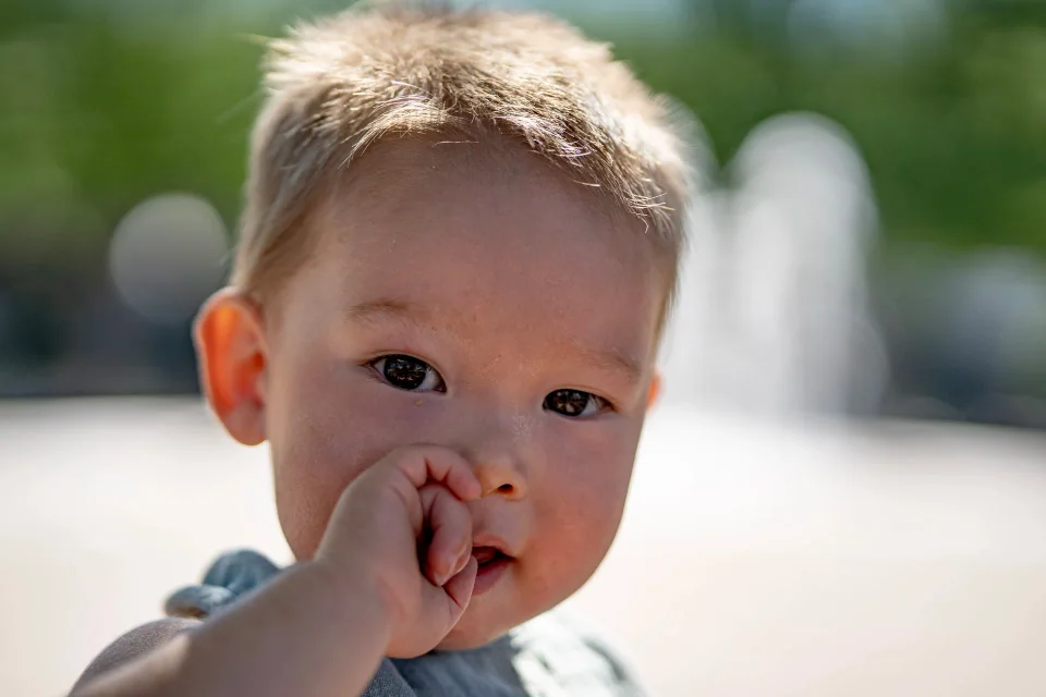 Close-up of a toddler looking toward the camera with a hand near their mouth