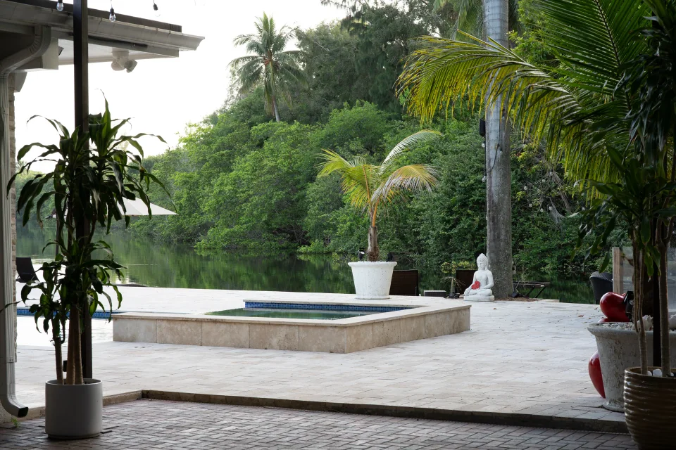 View from a covered patio across a pool toward a tropical garden