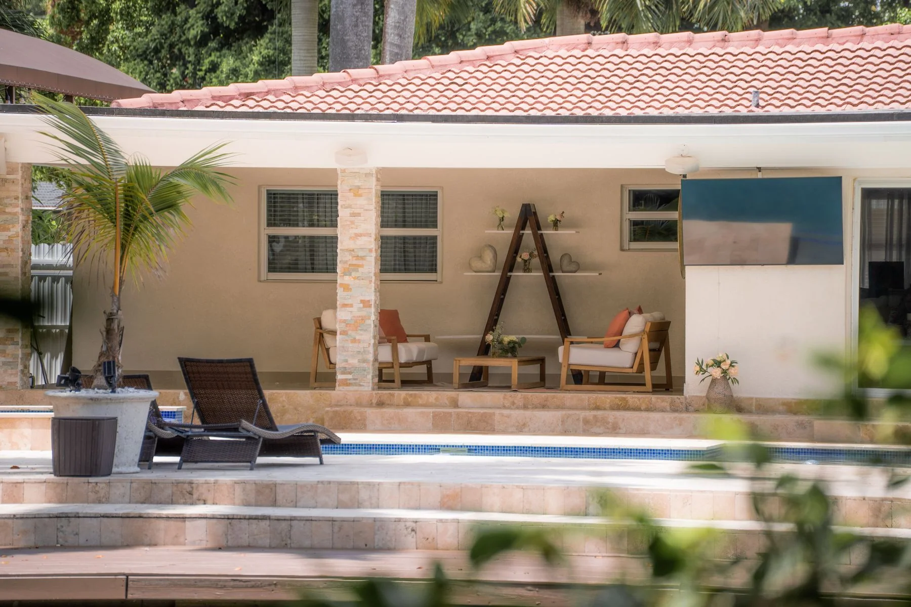 Poolside patio and covered lounge framed through foreground leaves