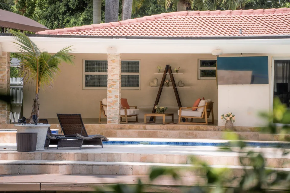 Poolside patio and covered lounge framed through foreground leaves