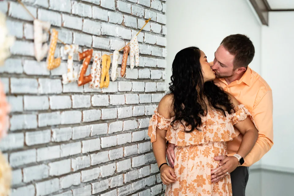 Couple embracing beside a white brick wall decorated for an event