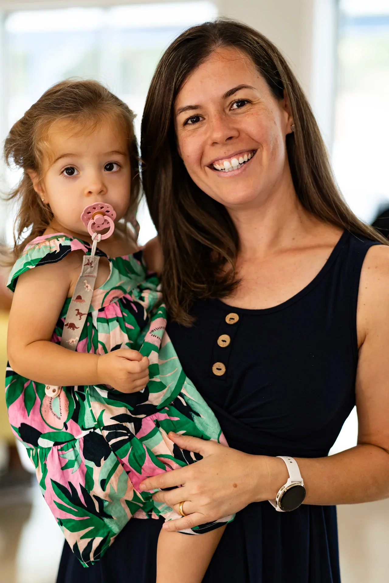 A smiling adult holding a toddler beside an indoor doorway