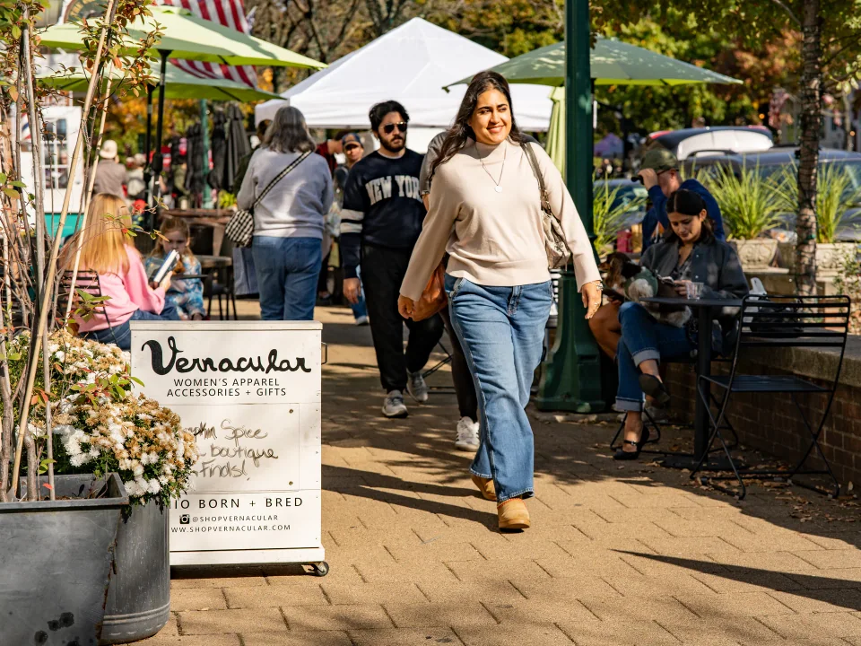 People walking past a flower display on a sunny brick sidewalk