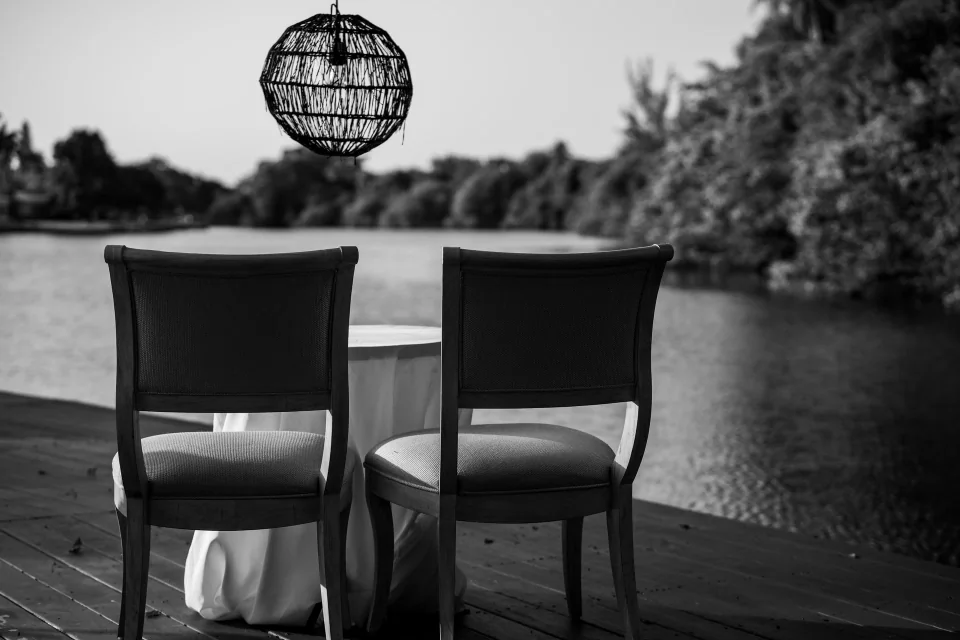 Two high-backed chairs on a waterfront deck, in black and white