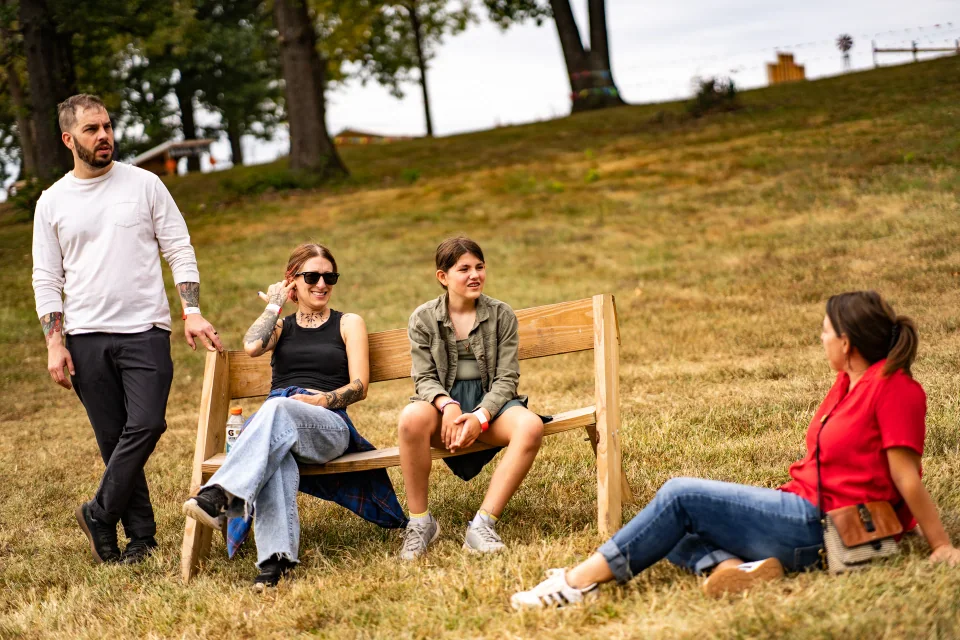 Four people spending time around a wooden bench on a grassy slope