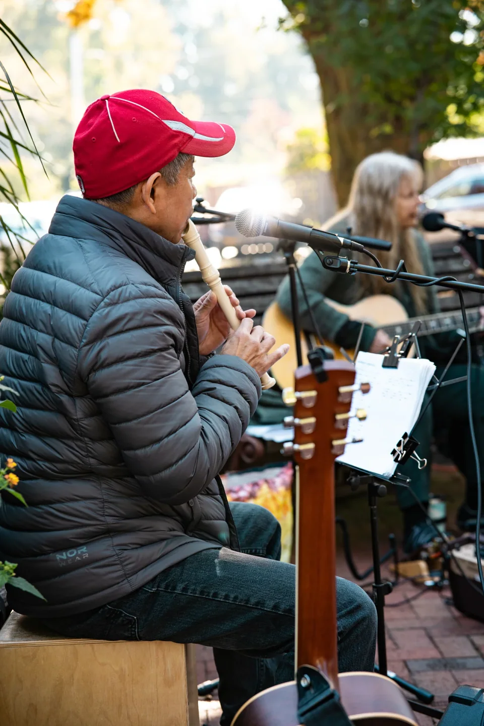 A seated musician wearing a red cap and playing a flute