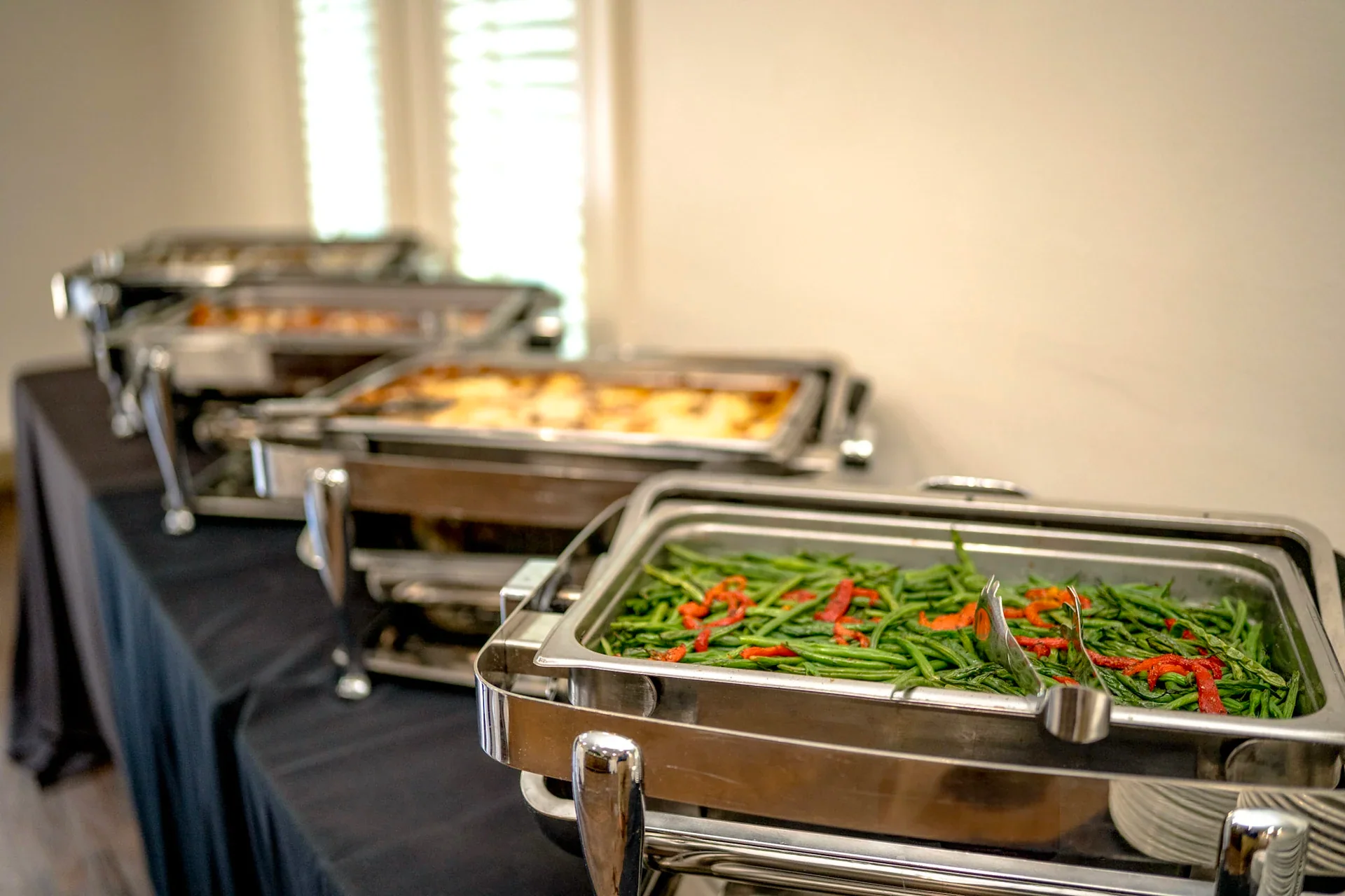 A catered buffet with covered serving trays and vegetables