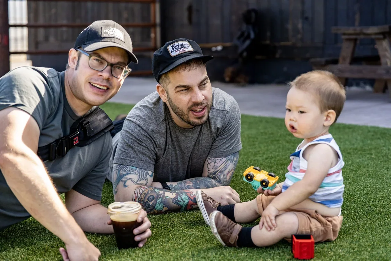 Two adults playing with a toddler and toys in a backyard
