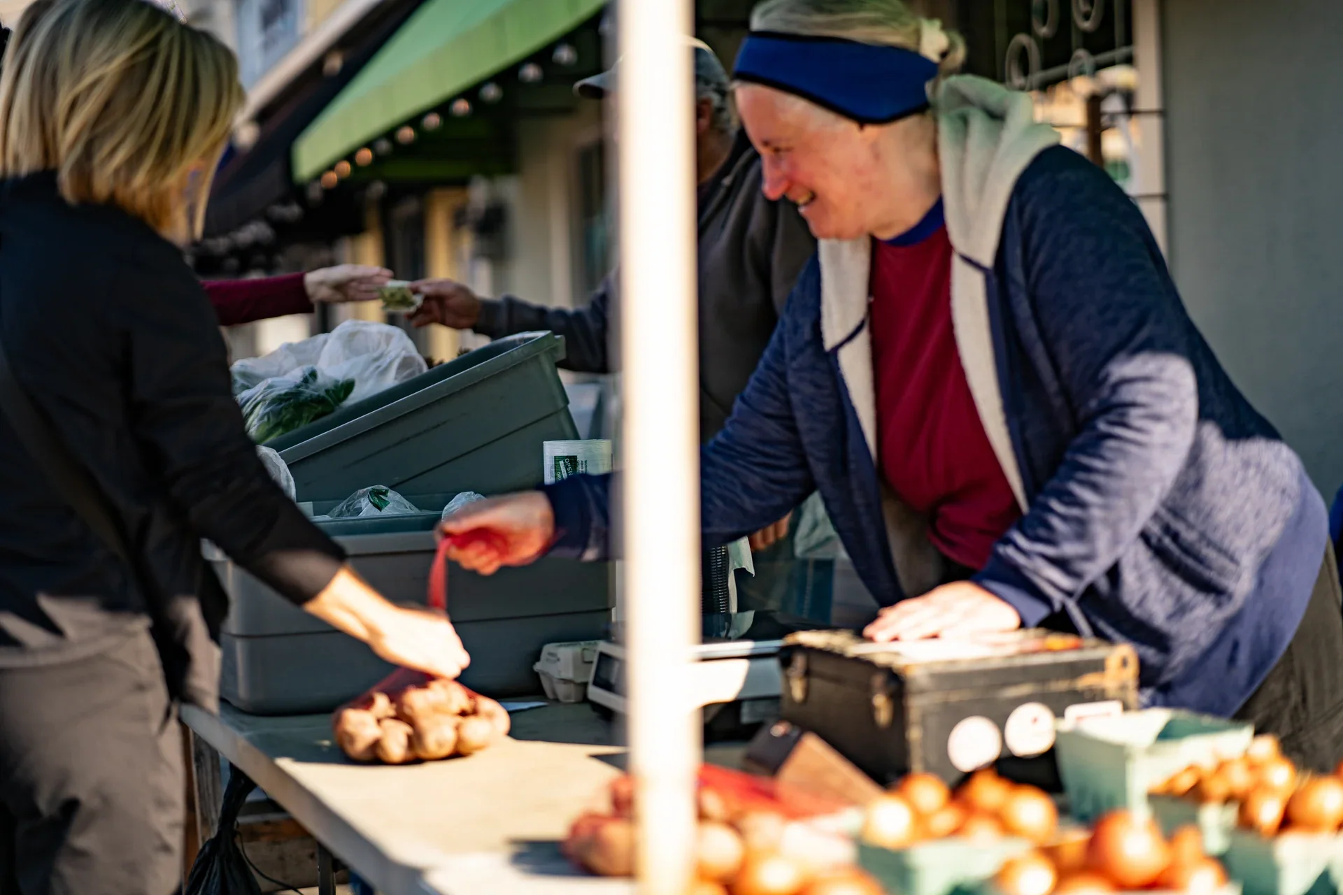 A vendor handing a small item across an outdoor market table