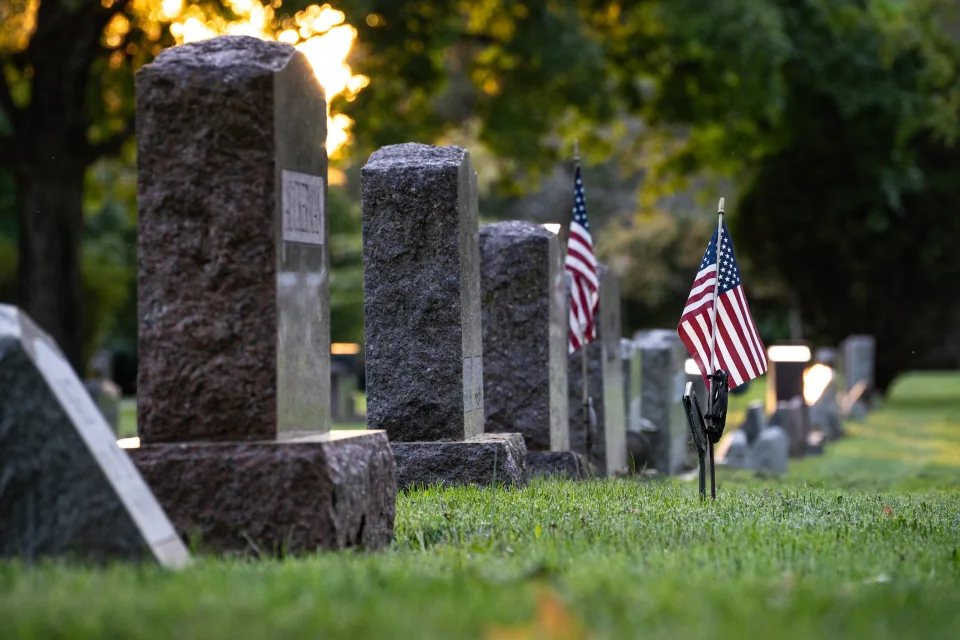 A row of gravestones with small American flags beneath trees